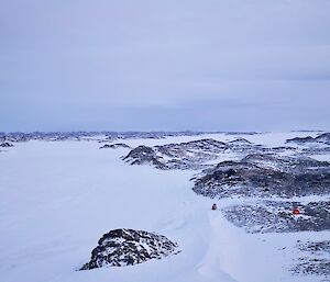 Looking down on to a snowy, frozen lake with a small red caravan just visible