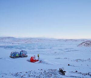 Snowy vista with a Hagglund next to a round, red caravan.  An expeditioner walks between them.