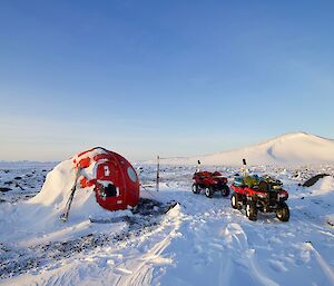 A round, red caravan with two quad bikes parked outside and skis leaning up against it