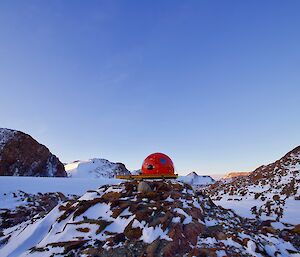 A round, red caravan in the middle of a rugged, snowy landscape