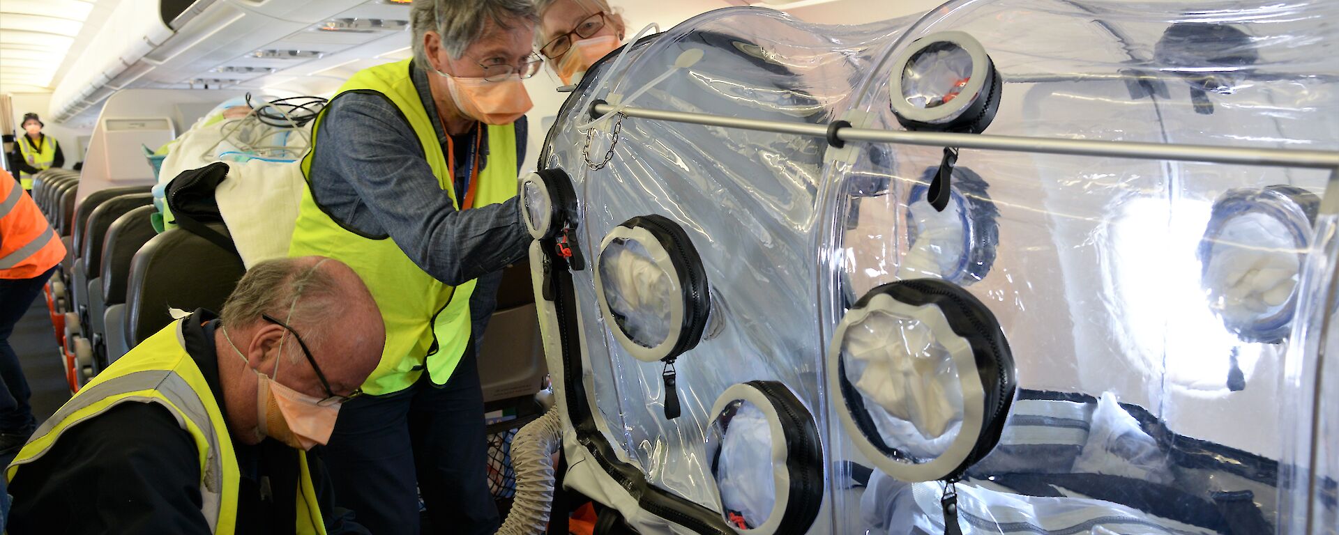 Three people on plane with clear plastic chamber