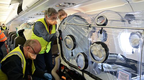 Three people on plane with clear plastic chamber