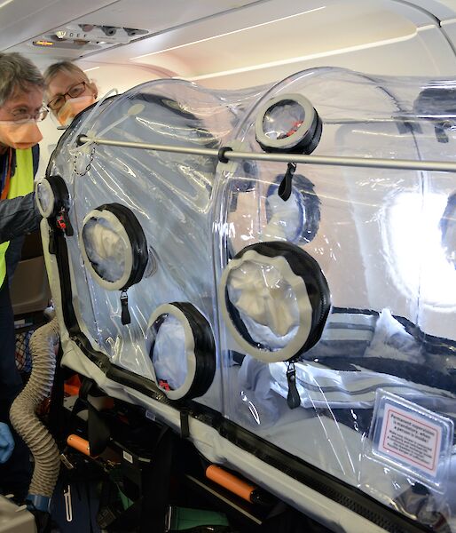 Three people on plane with clear plastic chamber