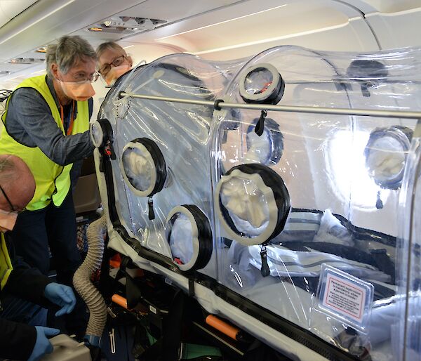 Three people on plane with clear plastic chamber