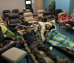 A theatrette style room with expeditioners lying in recliners with blankets