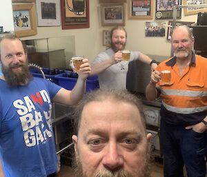 A selfie of 4 expeditioners holding up beer glasses and smiling to camera