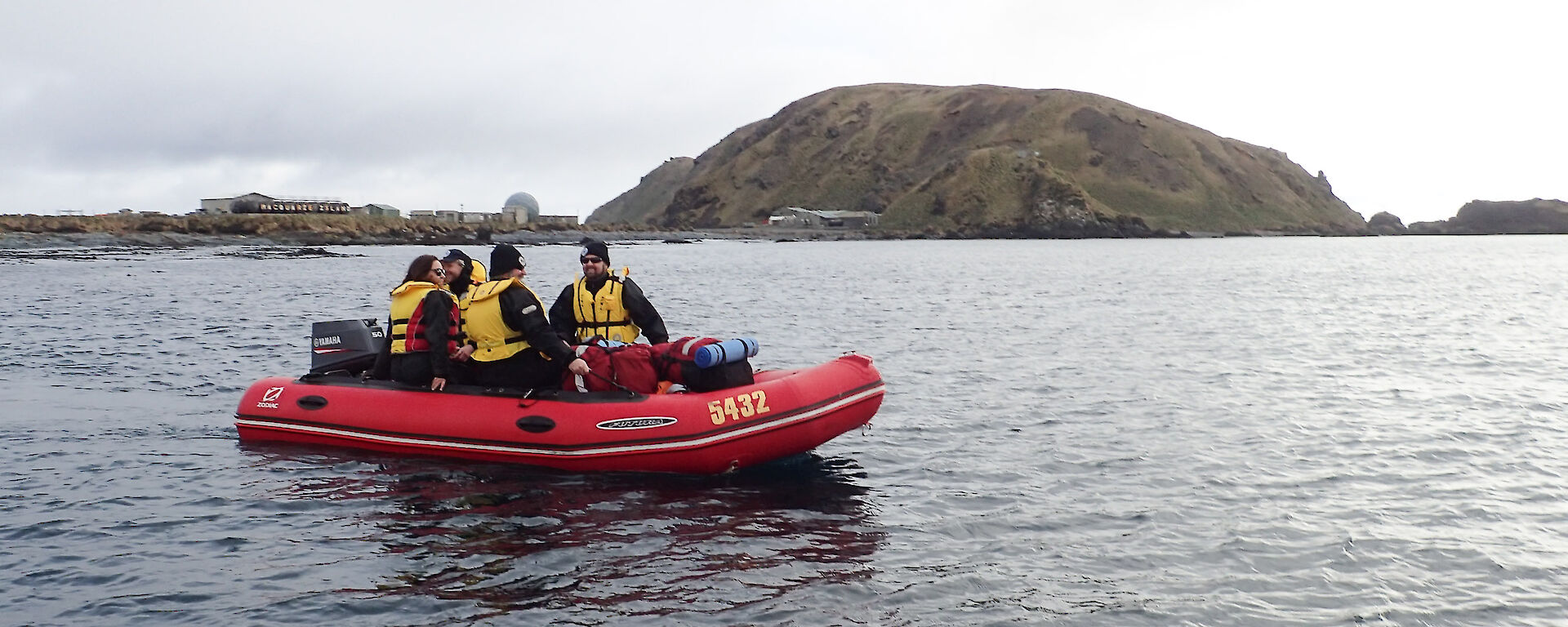 An IRB with expeditioners floating on the water. In the background The station and North Head can be seen,