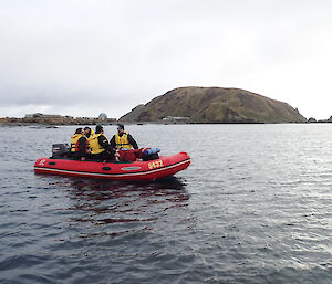 An IRB with expeditioners floating on the water. In the background The station and North Head can be seen,