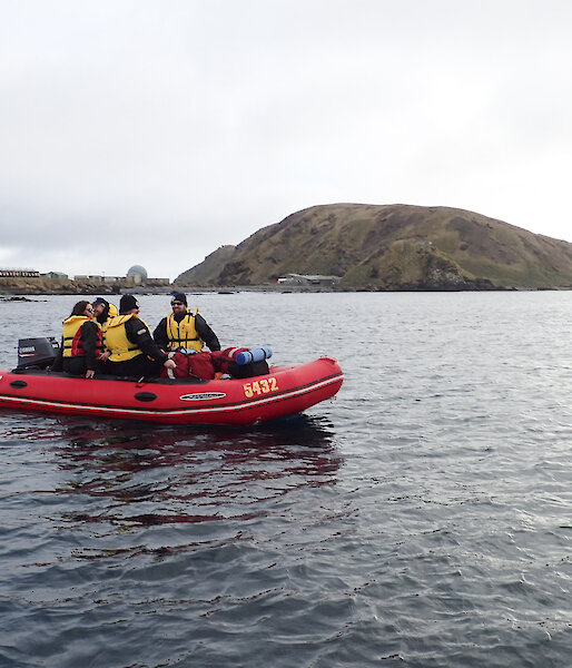 An IRB with expeditioners floating on the water. In the background The station and North Head can be seen,