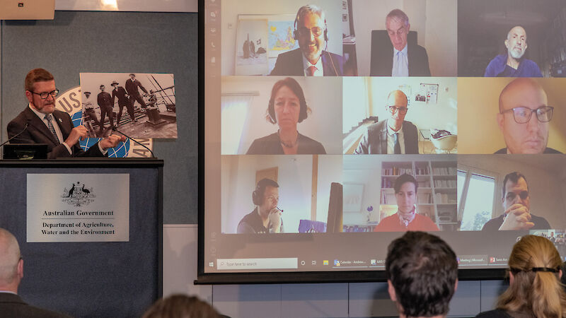 People on a giant screen, man standing next to it holding up a photograph