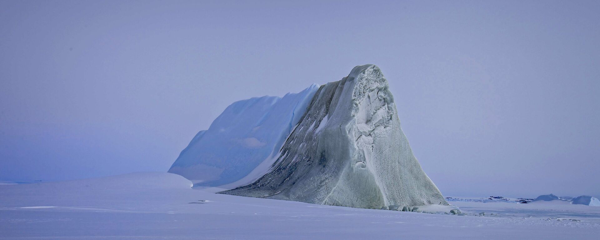 A jade iceberg in the middle of a snowy landscape, half covered in snow