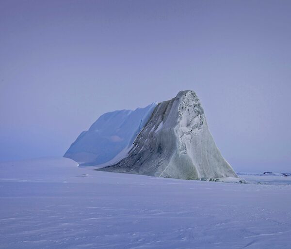 A jade iceberg in the middle of a snowy landscape, half covered in snow