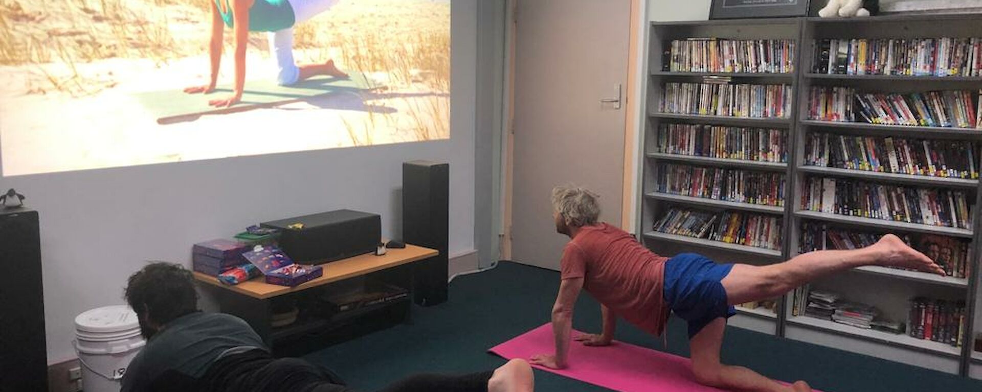 Two expedioners on yoga mats watching a yoga tutorial on screen and replicating the pose
