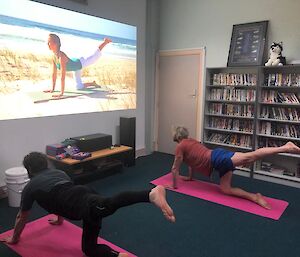 Two expedioners on yoga mats watching a yoga tutorial on screen and replicating the pose