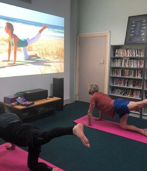 Two expedioners on yoga mats watching a yoga tutorial on screen and replicating the pose