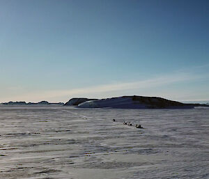 A aerial shot of a flat snowy landscape with a convoy of four vehicles just visible tracking towards the horizon