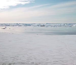 A snowy landscape looking towards the melted sea ice with bobbing icebergs