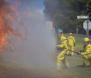 People with fire hose spray cloud of water against flames