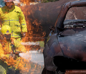 People in protective clothing with fire hose seen through flames