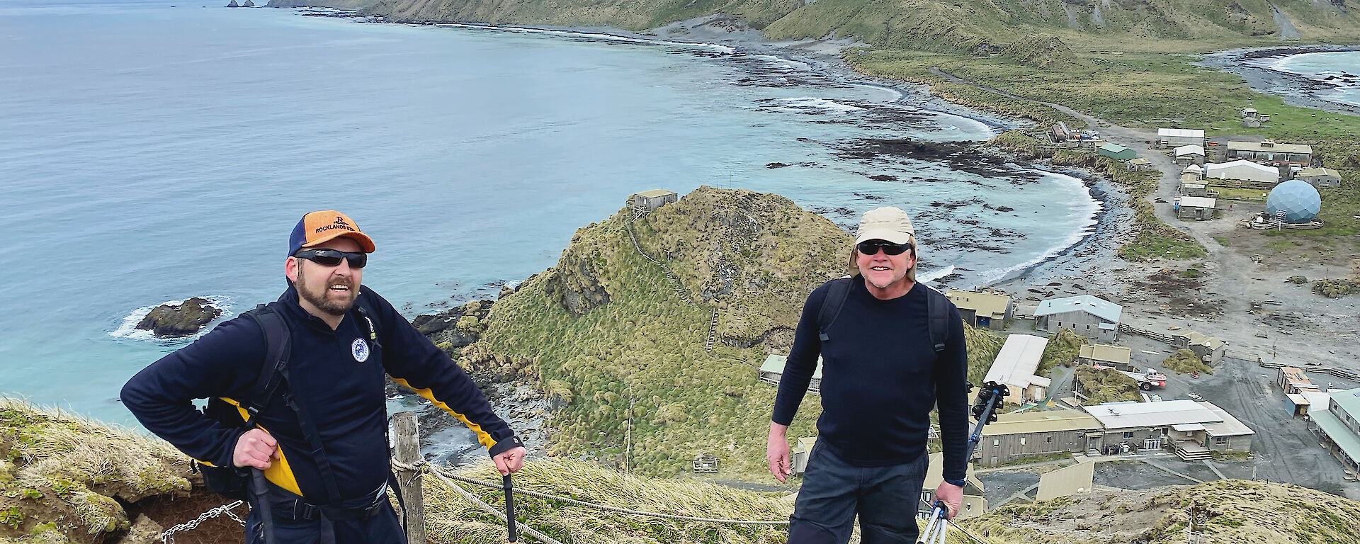 Two people standing at the top of hill with the sea, station and plateau behind them