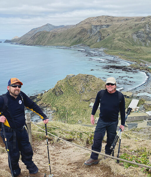 Two people standing at the top of hill with the sea, station and plateau behind them