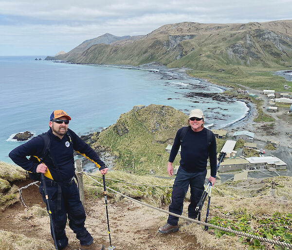 Two people standing at the top of hill with the sea, station and plateau behind them