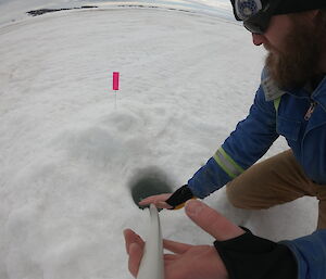 A man feeds a GoPro on a pole in to a hole in the ice