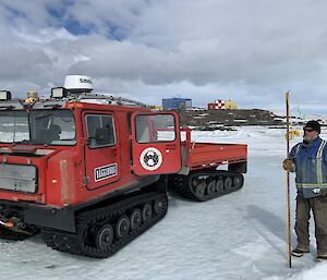 A man standing next to a Hagglund holding a pole