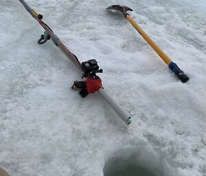 A camera on a pole an an ice pick next to a hole in the ice