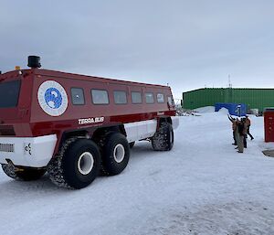 A red terra bus on the ice with expeditioners waving goodbye to the outgoing expeditioners visible through the bus windows