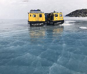 Two yellow Hagglunds on shiny sea ice with snow hill in the background