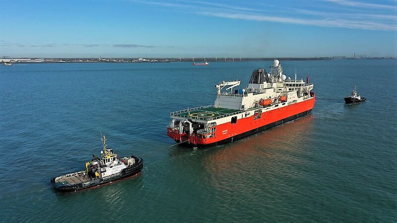 A red, white and black ice breaking ship, with two tug boats