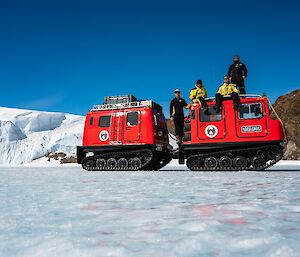 Two red Hagglunds on the ice with expeditioners sitting on the roof