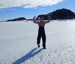 An expeditioner on the sea ice with his bare arms raised to the sky