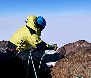 An expeditioner on the summit sitting on rocks holding the belay ropes