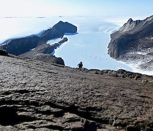 Looking down a rocky scree towards a climbing expeditioner.  The frozen lake and glacier are visible at the foot of the mountain.