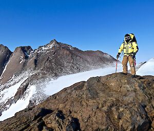 An expeditioner on top of a large rocky hill looking back to camera