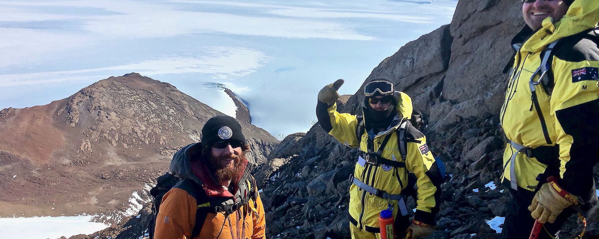 Three expeditioners smiling to camera near the summit of the mountain.  Glacier and snow below