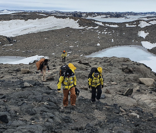 group of people walking in low rocky snowy hills