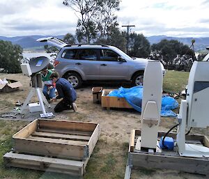 two men assemble equipment on hill top with car