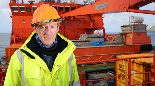Brad standing on the deck of the Aurora Australis in a hard hat and high vis jacket.
