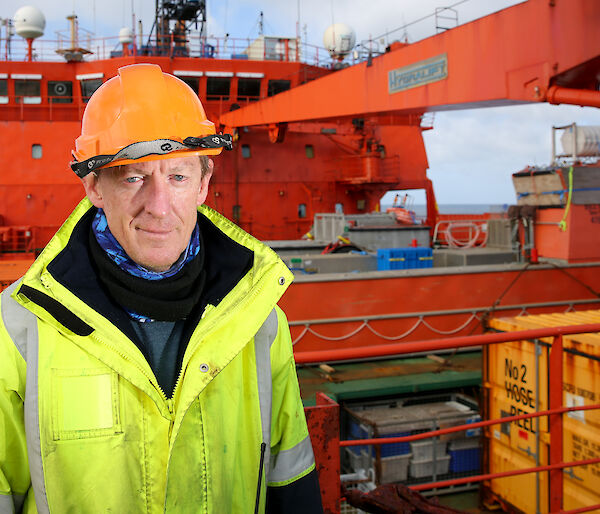 Brad standing on the deck of the Aurora Australis in a hard hat and high vis jacket.