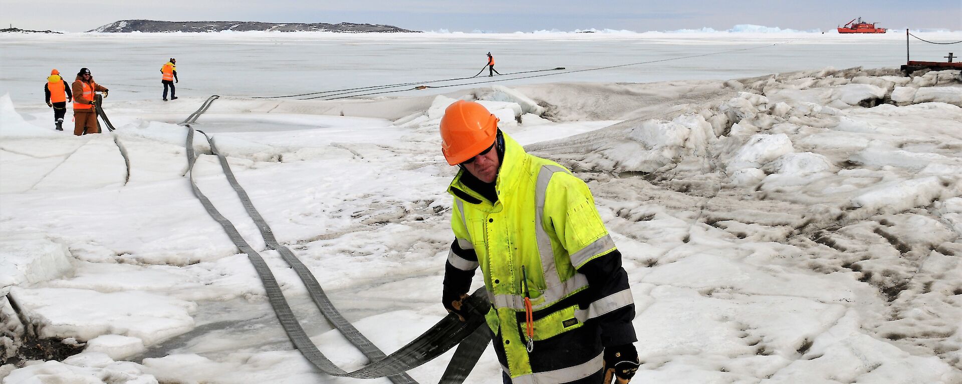 People dragging a length of fuel hose across the sea ice at Davis, Antarctica.