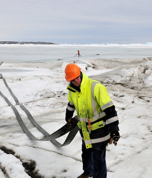 People dragging a length of fuel hose across the sea ice at Davis, Antarctica.