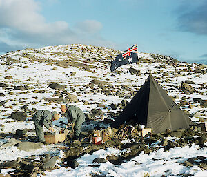 Two mean and tent with Australian flag on rocky snowy hillside