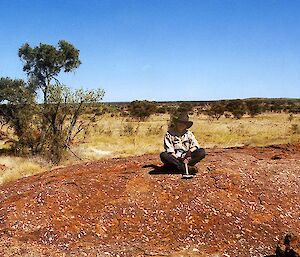 A woman sits alone on a red rock in the desert