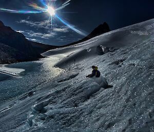 A night time shot of an expeditioner sitting half way up a slope with a frozen lake below him