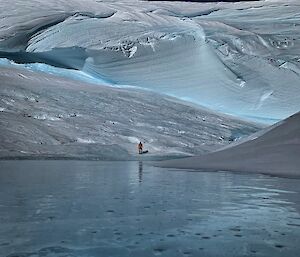 Wind scour lined by crystal clear frozen lake.  Expeditioner stands in middle of shot in the distance.