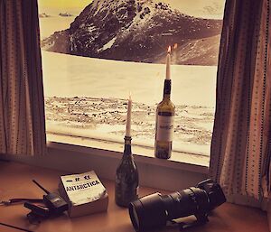 An arty shot of a cheese and meat platter, camera, radio, Antarctica book and candles, displayed looking out of a window at the snowy landscape