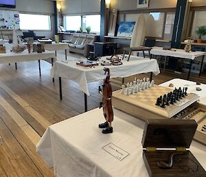 A room with tables covered in white table cloths. Various hand made art items are displayed on the tables.